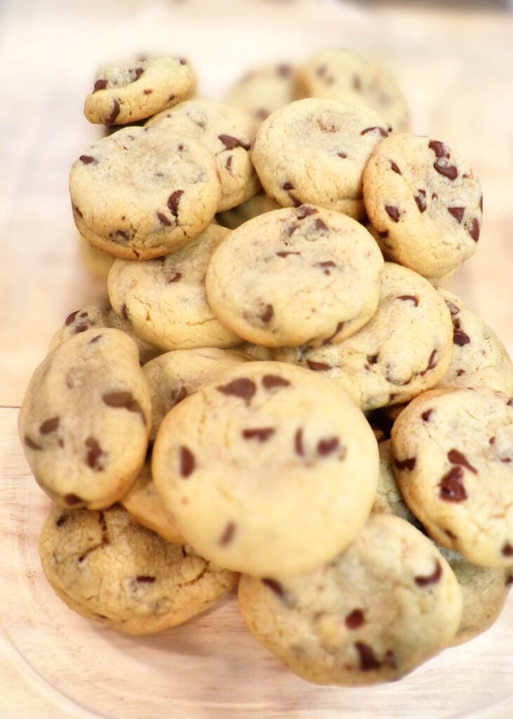 A pile of soft chocolate chip cookies on a wooden surface.