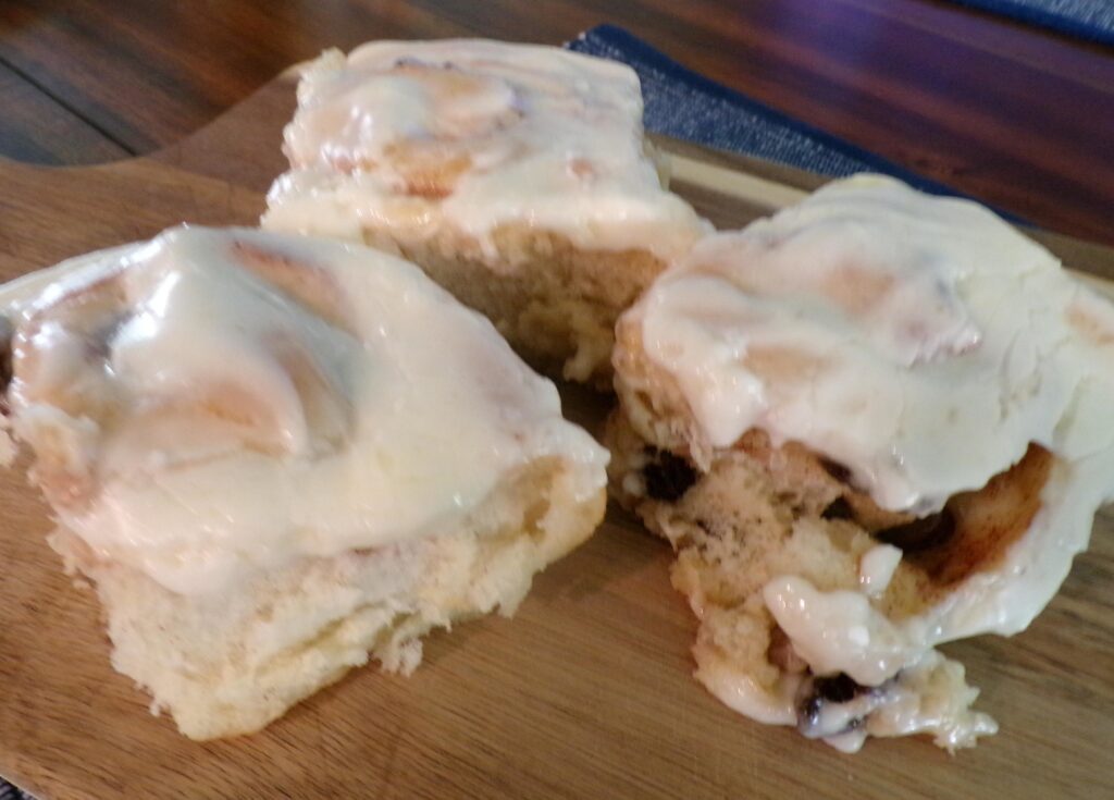 Three iced cinnamon rolls on a wooden board.