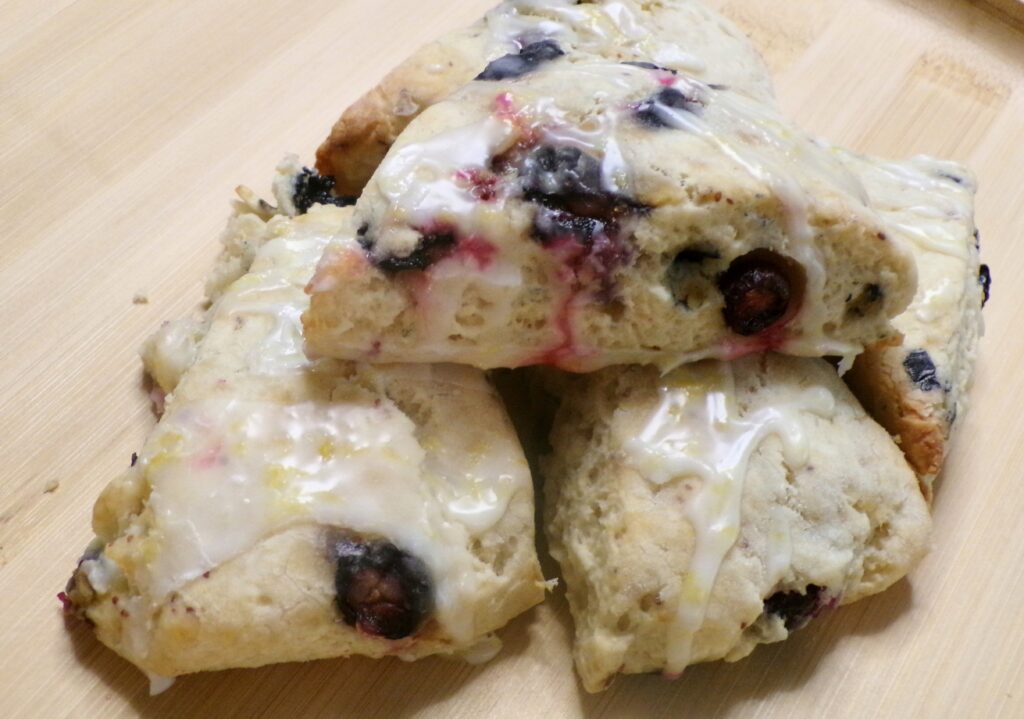 Three glazed blueberry scones on a wooden surface.