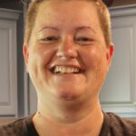 Smiling person with short hair in a kitchen.
