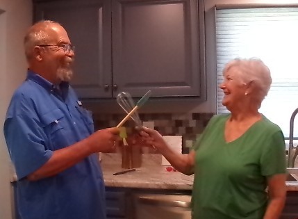 Two elderly people exchanging a gift in a kitchen.