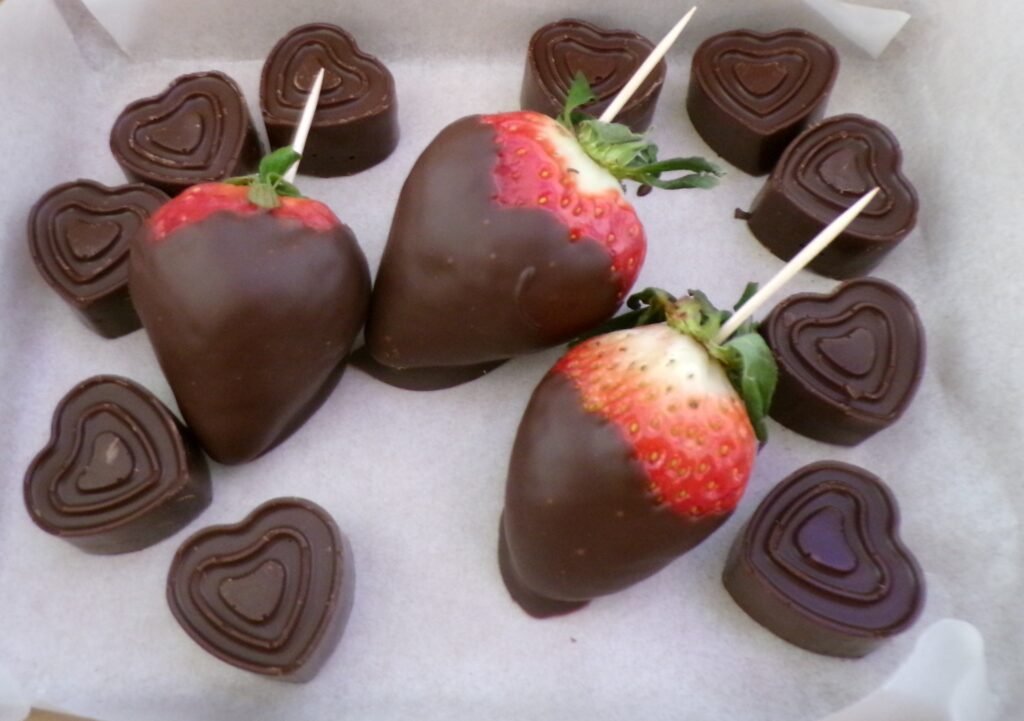Chocolate-covered strawberries and heart-shaped chocolates arranged on a white surface.